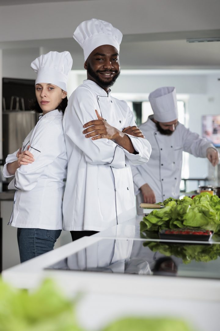 Multiethnic gastronomy experts standing in restaurant kitchen with arms crossed while posing at